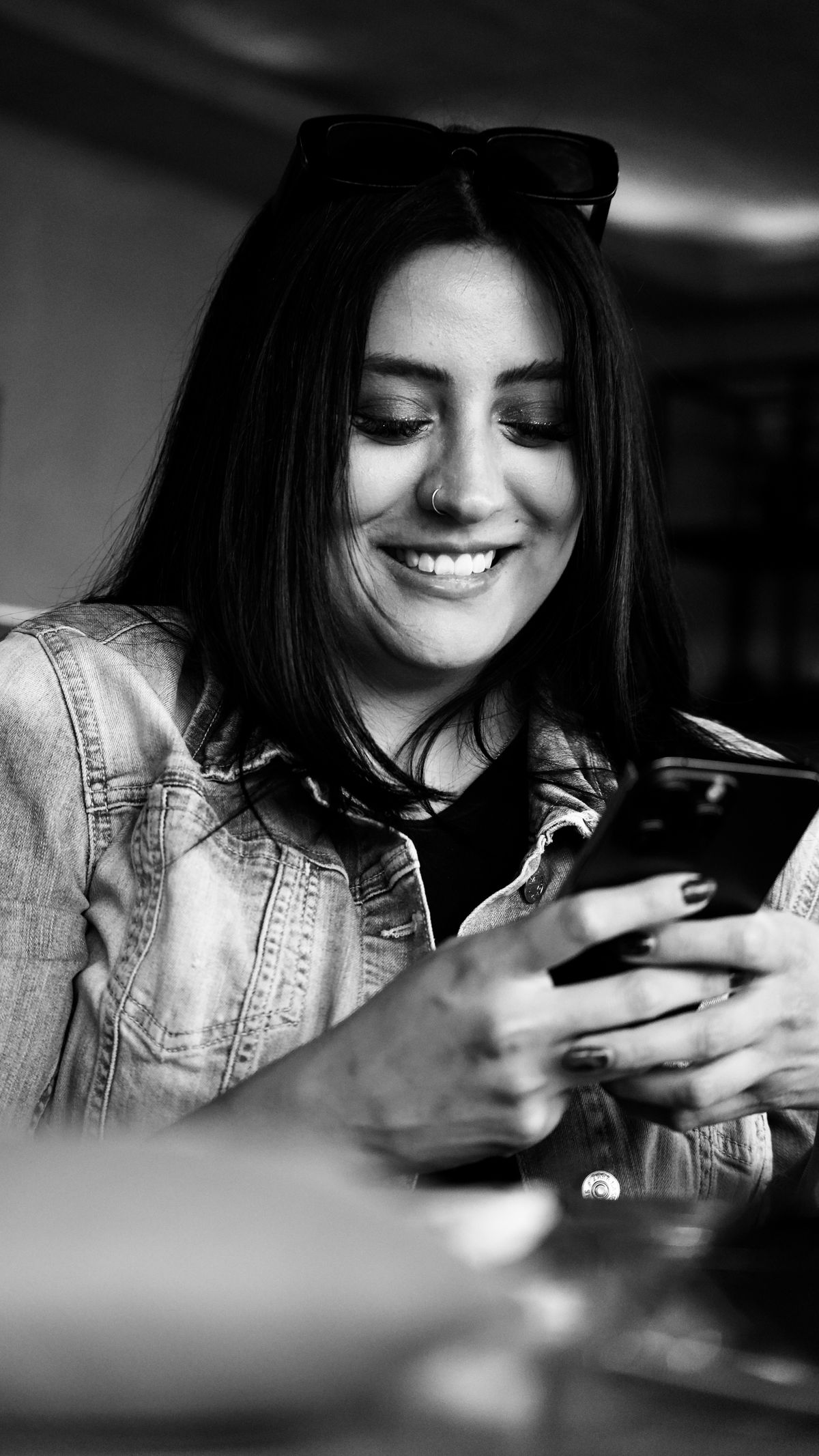 スマホでメッセージを打ちながら微笑む女性のモノクロ写真